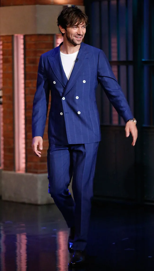 Man in a blue suit walks confidently on stage during a talk show appearance.
