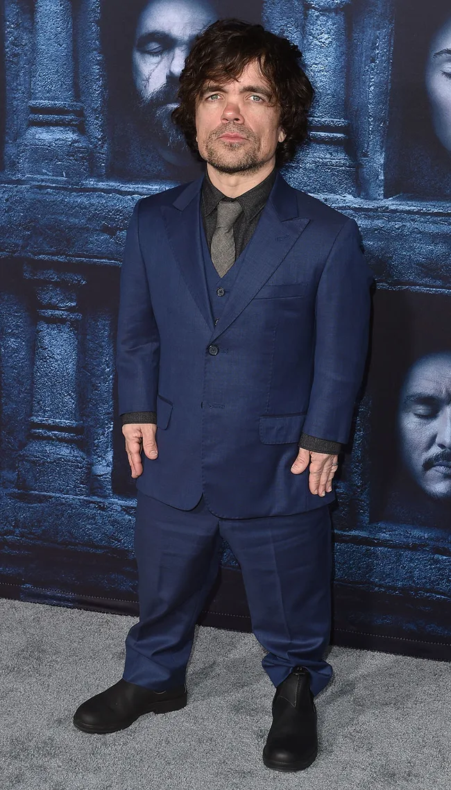 Man in a blue suit standing in front of a backdrop with face images.