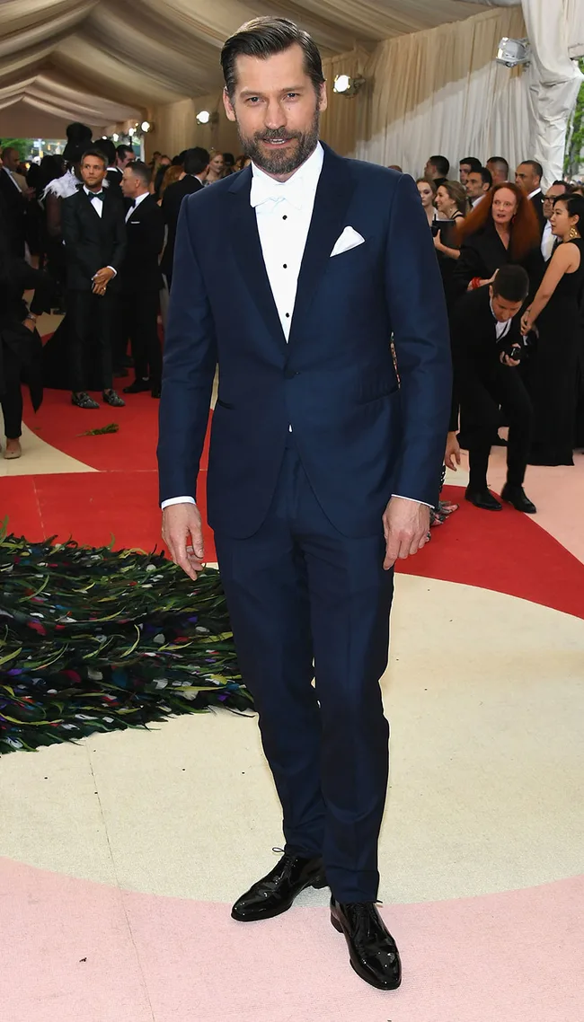 Man in a navy suit and bow tie at a formal event. Red carpet and crowd visible in background.
