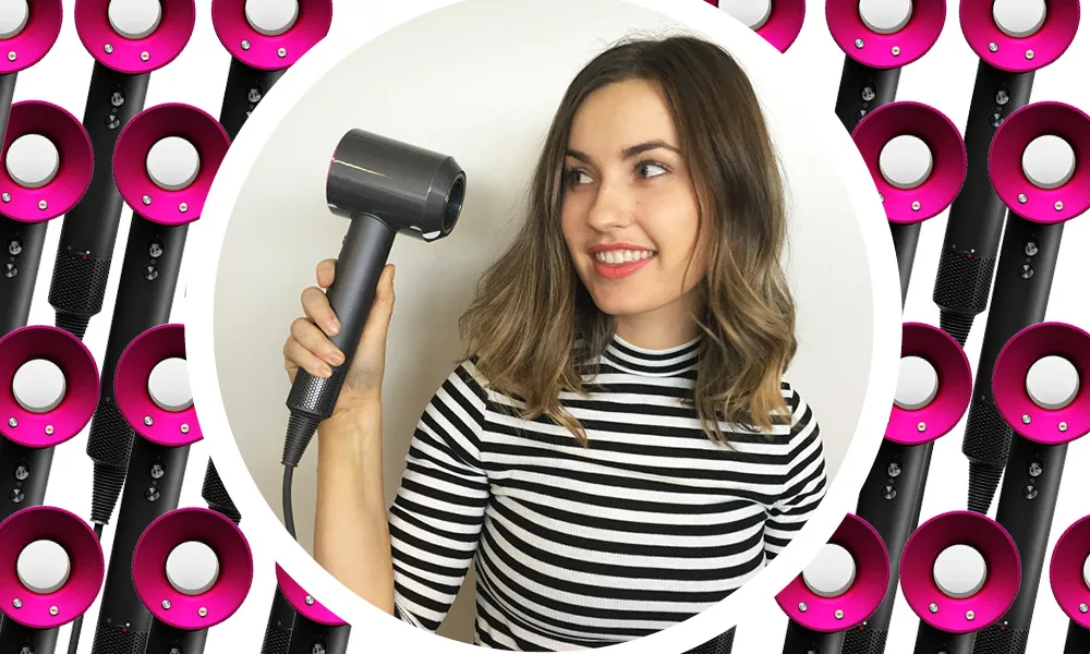 A woman holding a Dyson hair dryer smiles against a patterned background of more hair dryers.