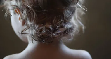 Back view of a toddler's head with curly hair against a soft-focus background.