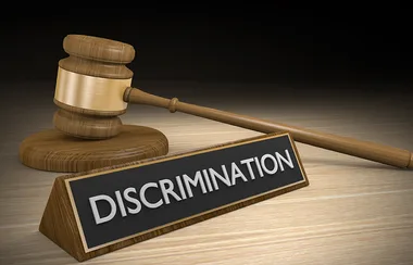 A wooden gavel next to a black plaque with the word "Discrimination" on a wooden surface.