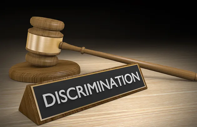 A wooden gavel next to a black plaque with the word "Discrimination" on a wooden surface.