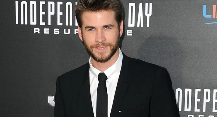 Man in a suit at the "Independence Day: Resurgence" premiere, standing against a movie-themed backdrop.