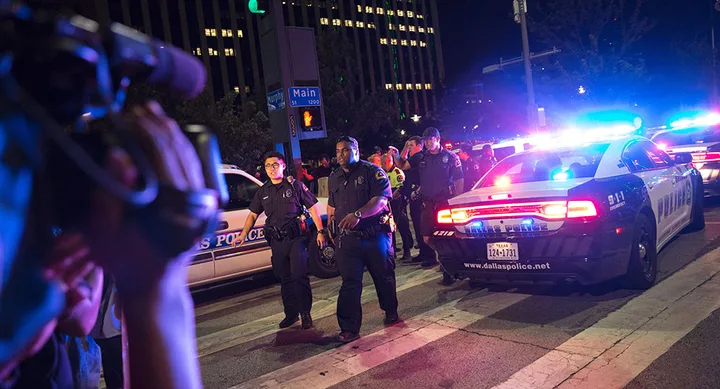 Police at a nighttime scene with flashing lights, vehicles, and people.