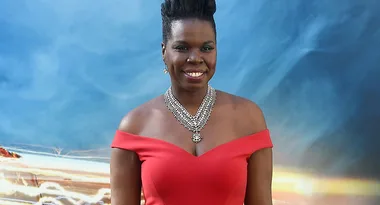 Woman in red dress and necklace smiling at a Ghostbusters movie premiere background.