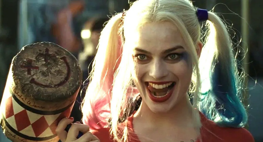 Harley Quinn with pigtails and a large mallet, smiling widely, makeup smeared.