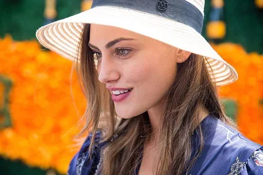 Young woman in a straw hat smiles, set against a vibrant floral background.