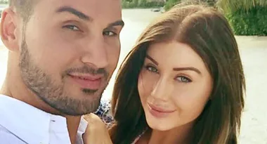 A couple smiling outdoors, with tropical greenery in the background.