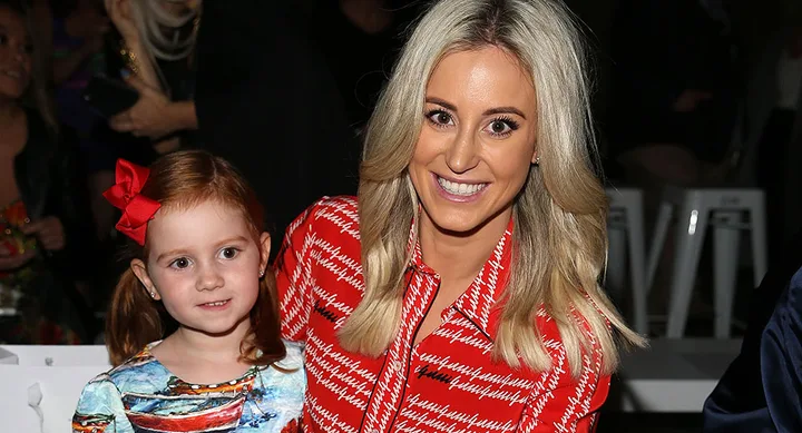 A woman in a red patterned dress smiling beside a young girl with a red bow, seated together.