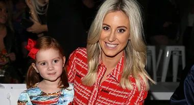 A woman in a red patterned dress smiling beside a young girl with a red bow, seated together.