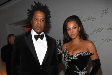 A man in a black tuxedo beside a woman in an ornate black dress pose for a photo at a formal event.