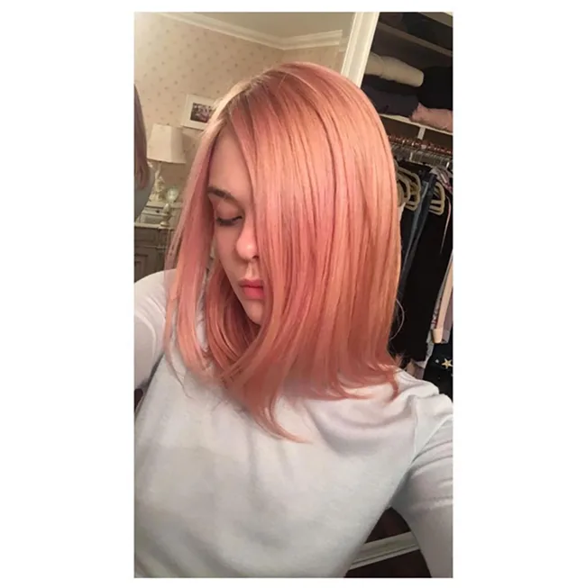 Person with shoulder-length pink hair looking down in a room with a closet in the background.