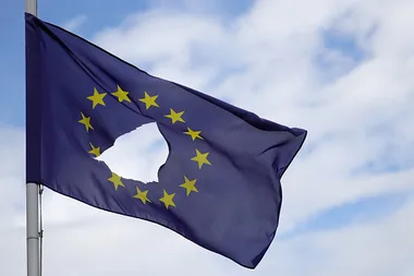 European Union flag with a hole in the center, missing stars, waving against a cloudy sky.
