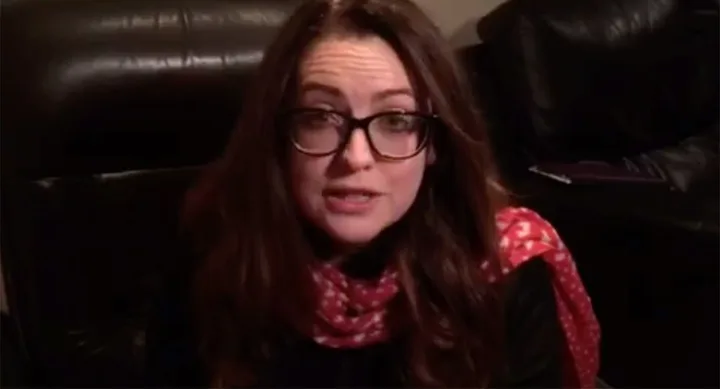 Woman with glasses wearing a red scarf, sitting on a black leather couch.
