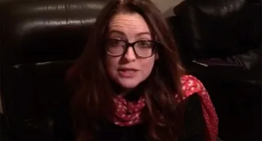 Woman with glasses wearing a red scarf, sitting on a black leather couch.