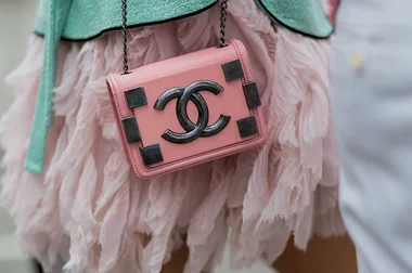 A pink Chanel bag with black metal accents against a pink ruffled skirt and turquoise fabric.