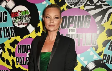 A person in a green dress and black blazer stands in front of a colorful "Hoping for Palestine" backdrop.