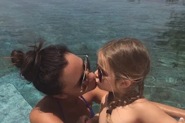 A woman and a child wearing sunglasses share a kiss in a pool.