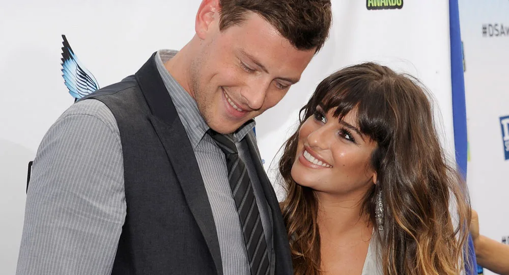 ```html
<img src="your-image-url.jpg" alt="Two people smiling on a red carpet, exchanging a warm look at an event." />
```