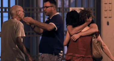 Group of four people: two men talking seriously, woman hugging another person with her hand on their head, evening setting.