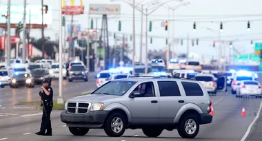 A police officer stands near an SUV on a blocked highway with flashing lights, indicating a traffic stop or incident.