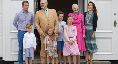 Seven people, including children, smiling in front of a building with large white doors.