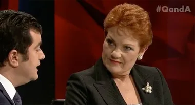 Two people engaged in conversation on a TV show set, with a #QandA hashtag visible in the top-right corner.