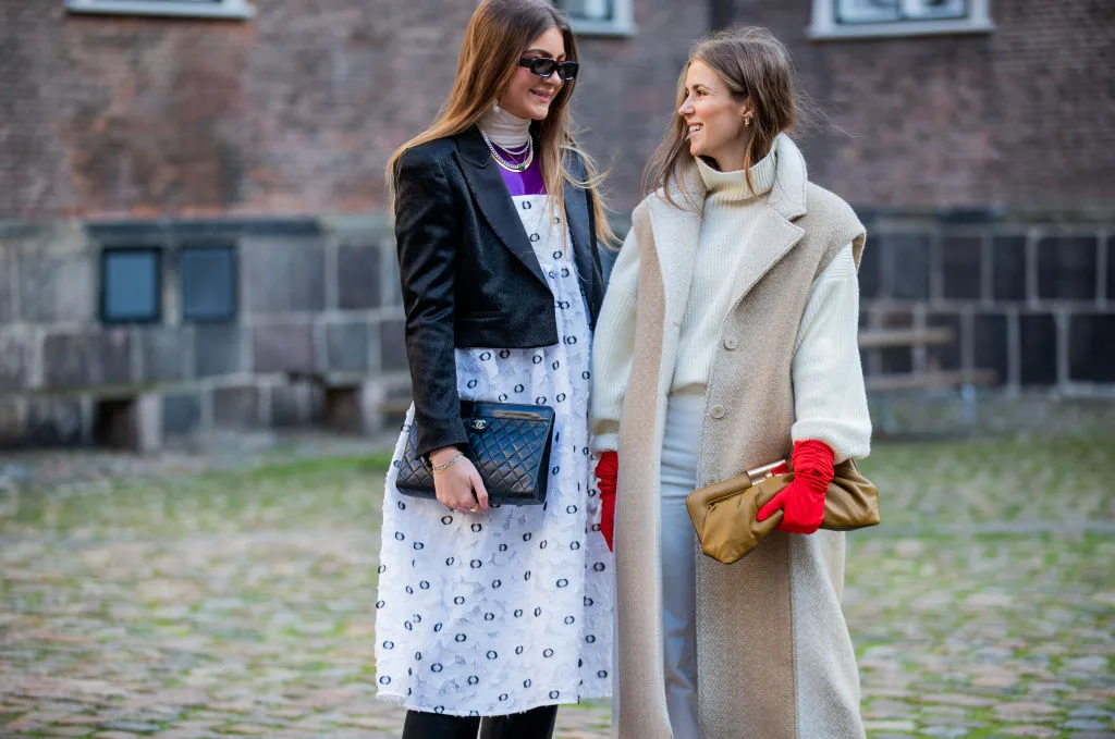 Maren Schia wearing dress with print, cropped jacket, Chanel bag and Nina Sandbech is seen wearing sleeveless coat, red gloves, brown clutch, turtleneck, white pants, two tone red white ankle boots outside Mfpen