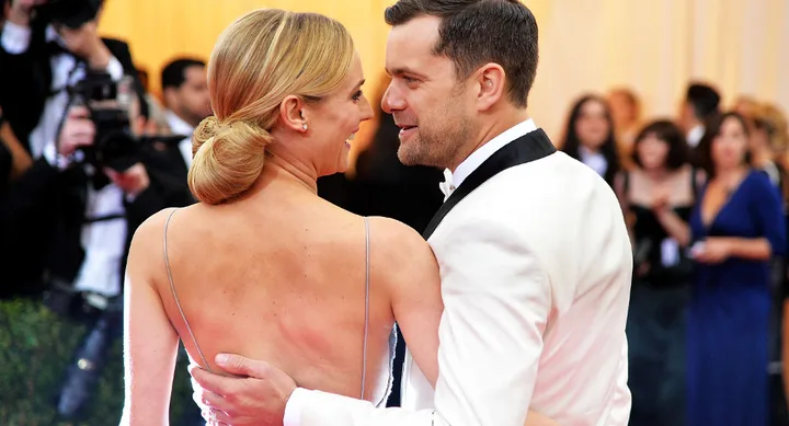 A couple embracing at a formal event with photographers and guests in the background.