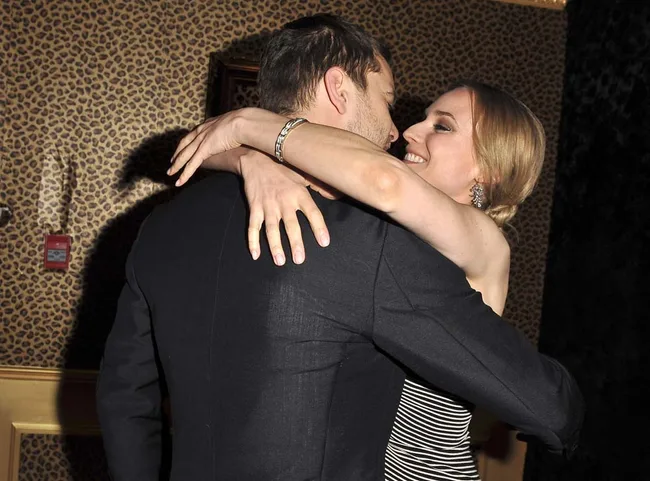 Two people embracing warmly, smiling at each other in a room with leopard print wallpaper.