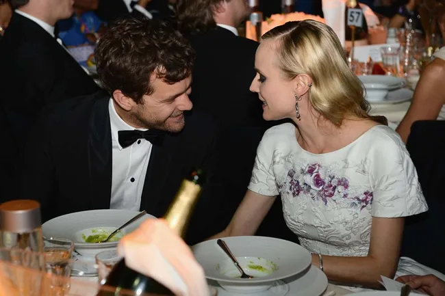 Two people in formal attire smiling at each other at a gala dinner table with plates and glasses.