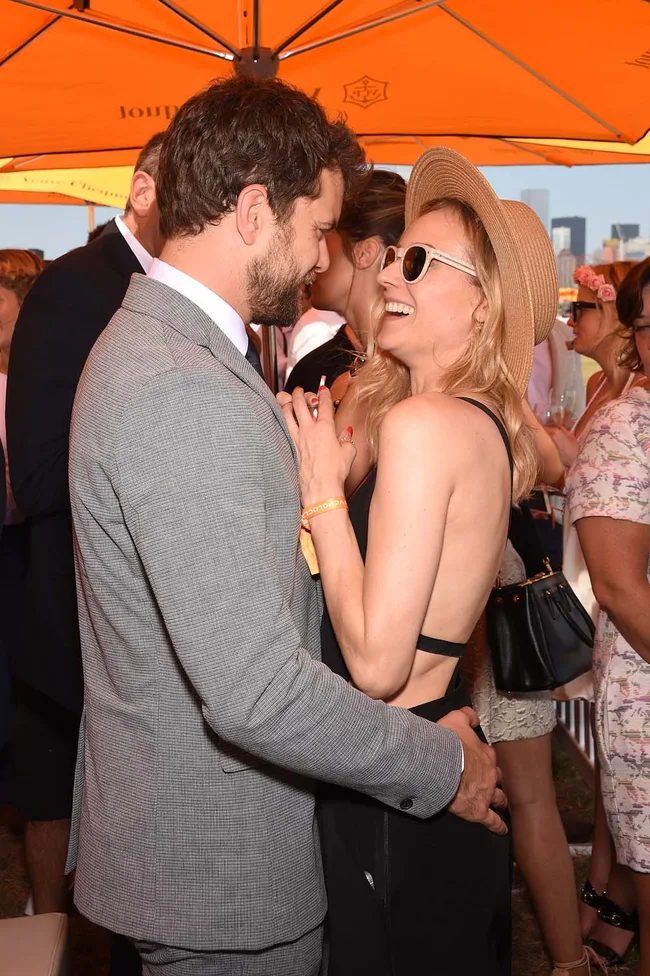 A couple laughing and embracing under an orange umbrella at an outdoor event.