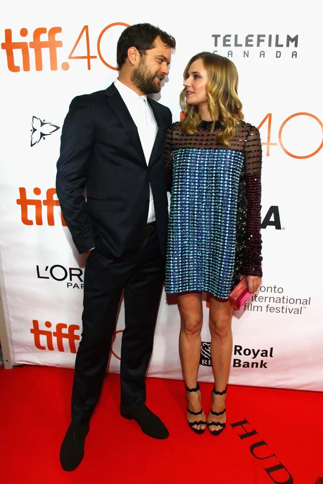 A man and woman on the red carpet at TIFF 40, with logos in the background, wearing a suit and a sparkly dress.