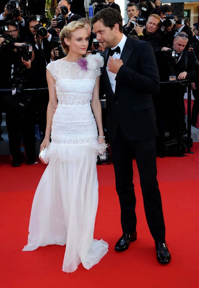 Couple in formal attire on a red carpet surrounded by photographers.