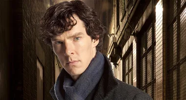 Man in a dark coat and scarf stands in a dimly lit alleyway, looking serious and focused.