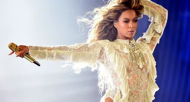 Singer performs on stage in a sparkling, ornate costume, holding a microphone with lighting creating a dynamic effect.