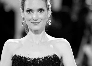 Black and white image of a woman in an elegant strapless dress and earrings, smiling at an event.