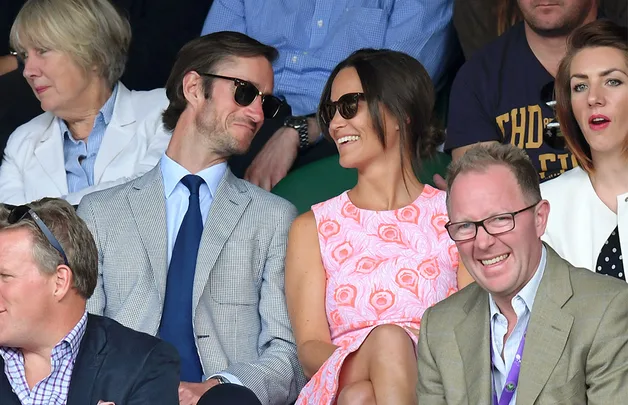 Spectators at an outdoor event, smiling and wearing sunglasses, enjoying the moment.
