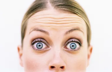 Close-up of a person's eyes wide open with raised eyebrows and visible forehead lines.