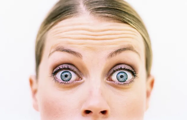 Close-up of a person's eyes wide open with raised eyebrows and visible forehead lines.
