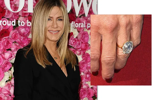 "Person smiling in front of floral backdrop with a close-up showing a large diamond ring on their hand."