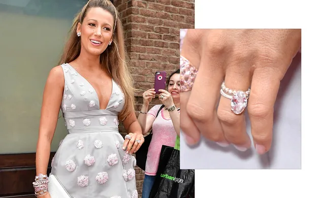 Elegant woman in a floral dress showing an oval diamond ring, smiling at an outdoor event, with onlookers capturing photos.