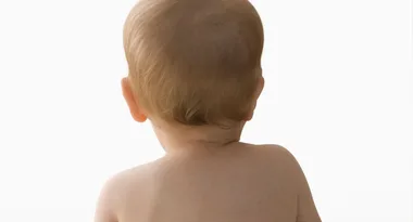 Back view of a baby with light brown hair against a plain white background.