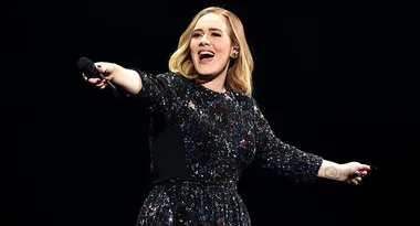 Singer performing on stage in a glittery dress, holding a microphone with an arm outstretched.