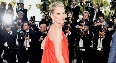 A woman in a red dress poses on the red carpet, surrounded by photographers at an event.