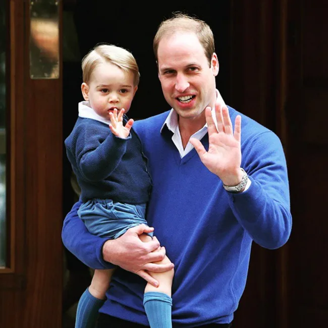 Father holding a young boy, both wearing blue and waving at the camera.
