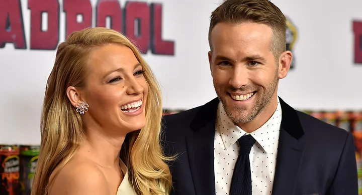 A smiling couple at a movie premiere event, with the "Deadpool" logo visible in the background.