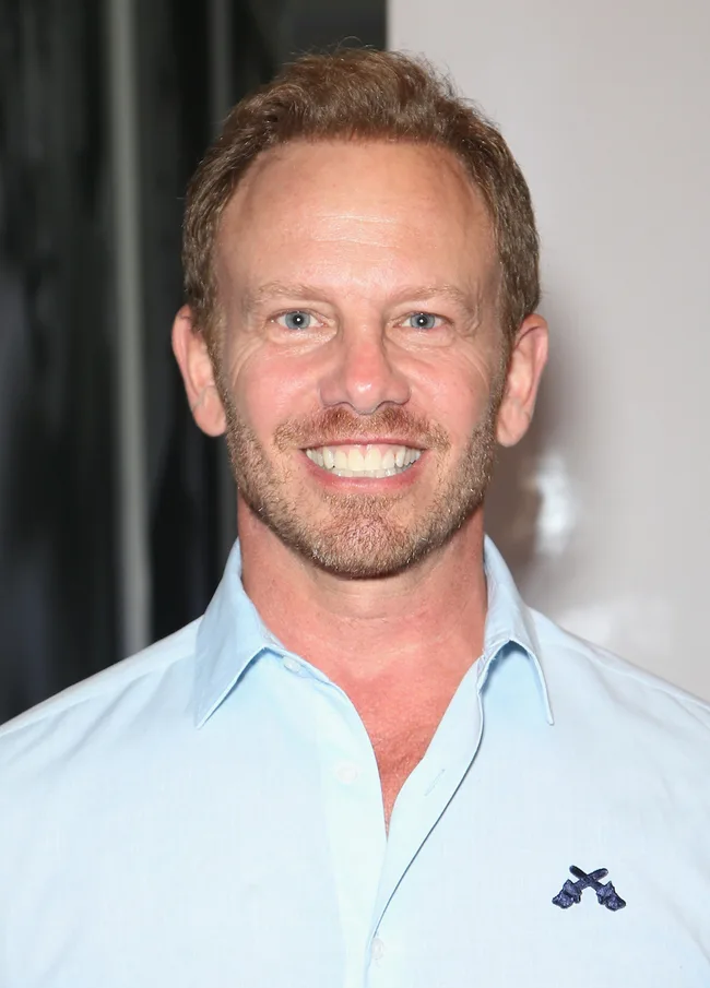 A smiling man with short hair and a beard in a light blue shirt.