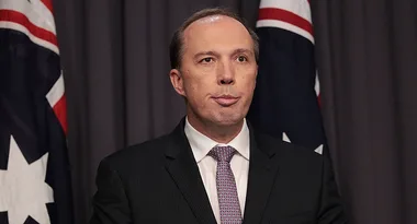 A man in a suit speaks at a podium with Australian flags in the background.